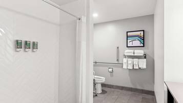 Un baño moderno con ducha, inodoro y barras de apoyo. Hay tres secamanos fijos en la pared.