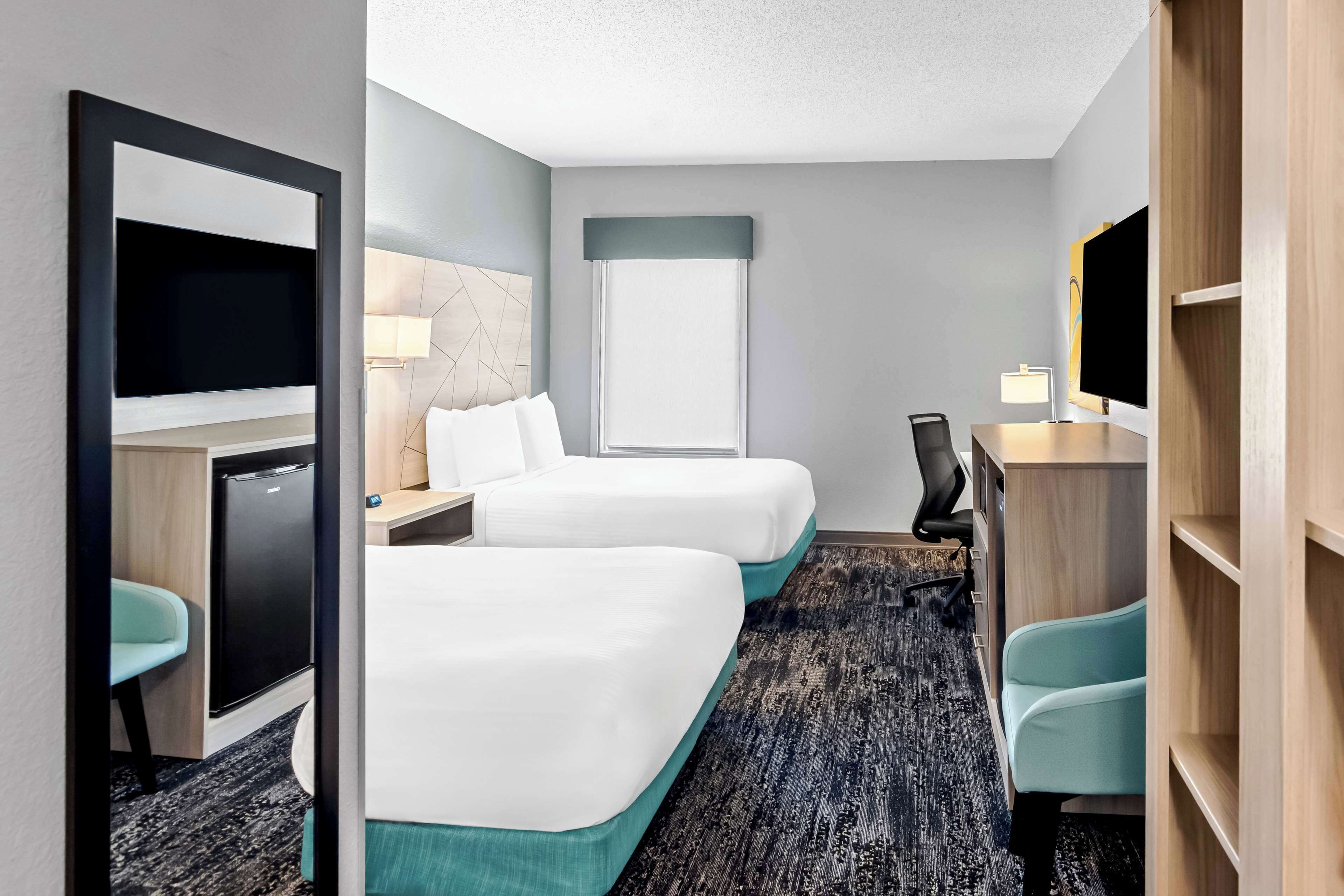 A hotel room with two beds, a desk, a chair, a TV, a lamp, and a wardrobe.