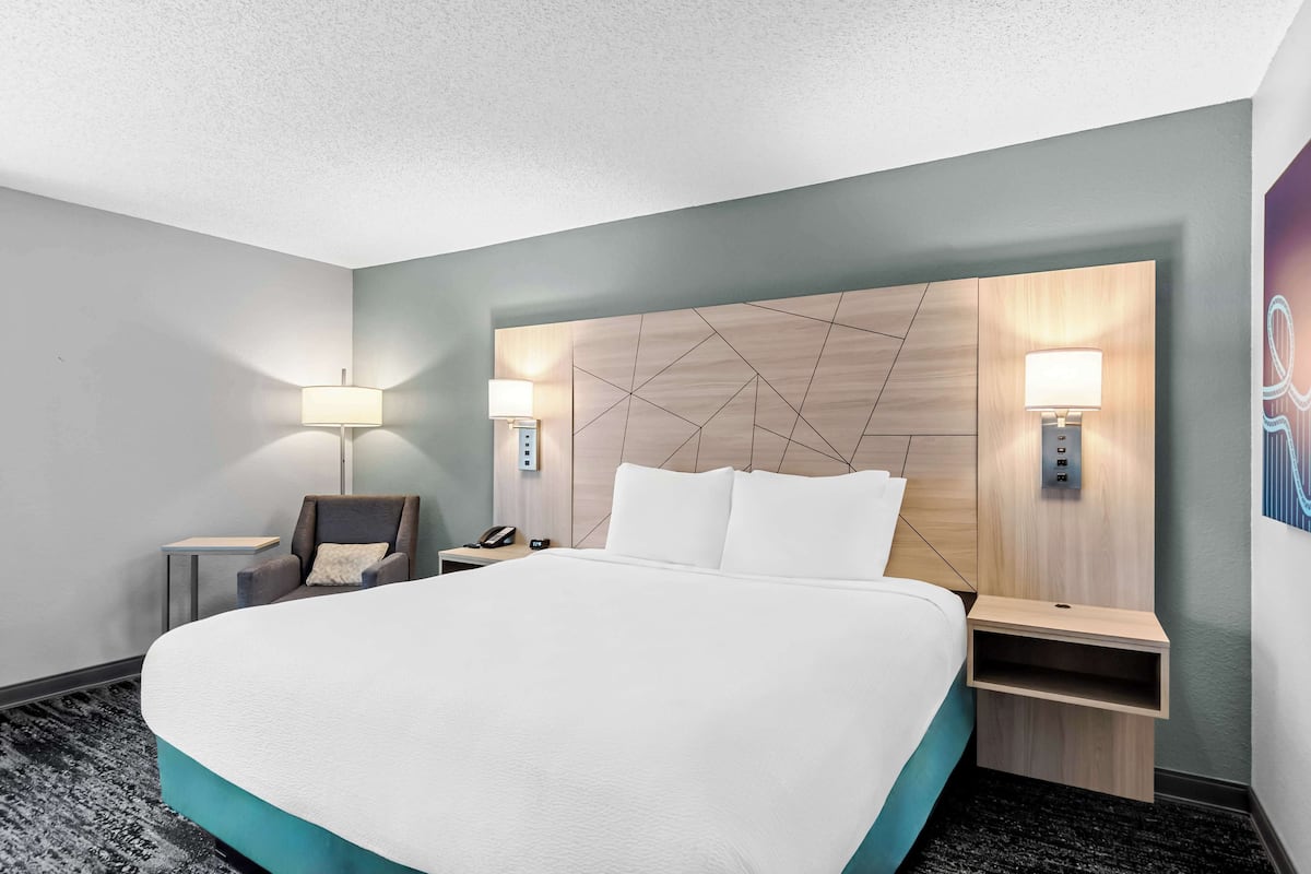 A hotel room with a large bed, two bedside tables with lamps, a chair, and a wall-mounted phone.