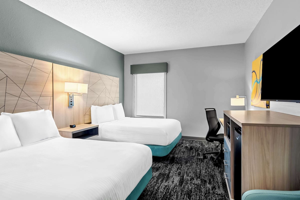A hotel room with two beds, a desk, a chair, a TV, and a window with a curtain.