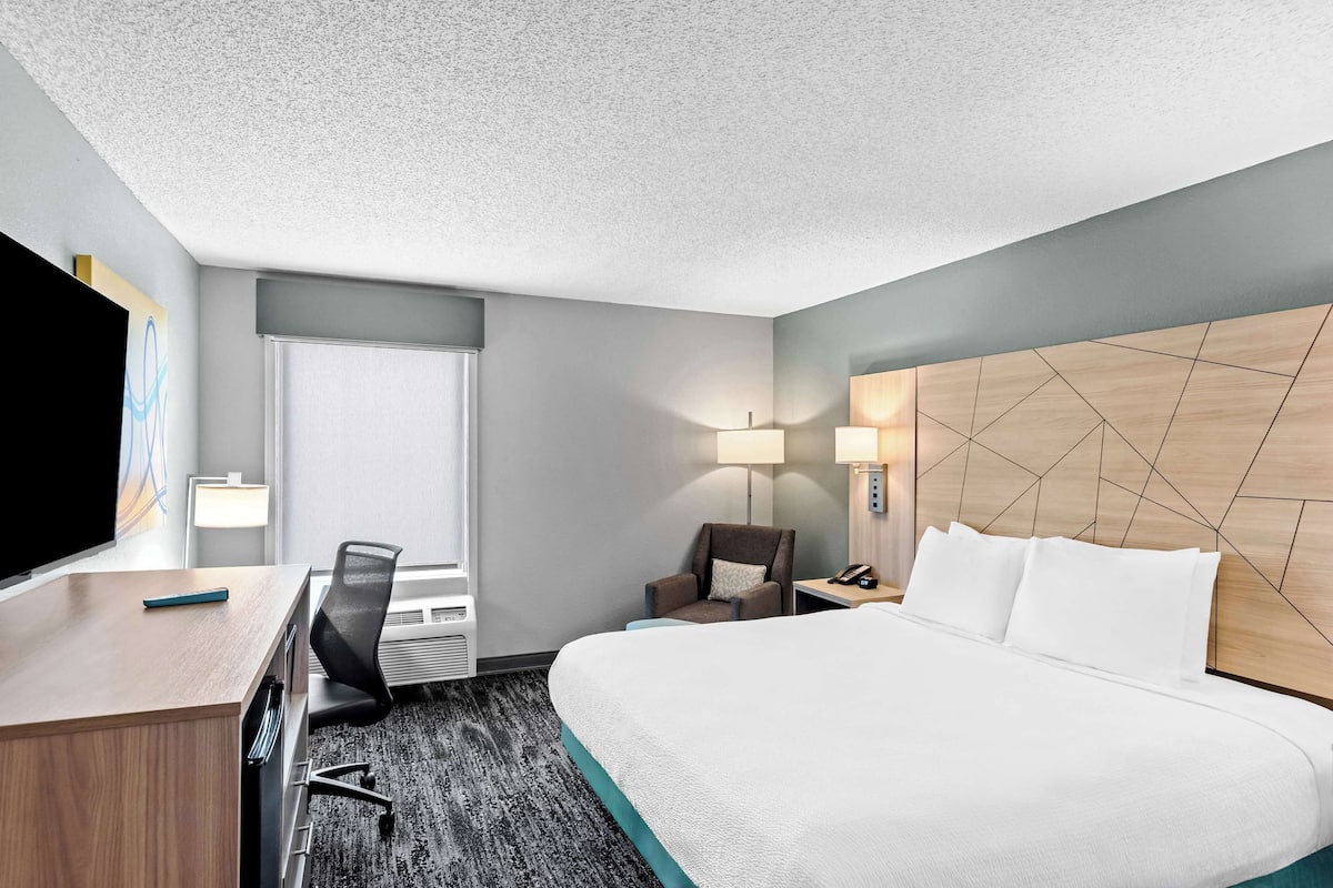A hotel room with a bed, desk, chair, and a TV.