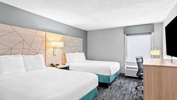 A hotel room with two beds, a desk, a chair, a lamp, and a window.