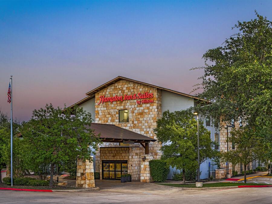 Um hotel com fachada de pedra e uma placa com a inscrição 'Hampton Inn & Suites by Hilton'.