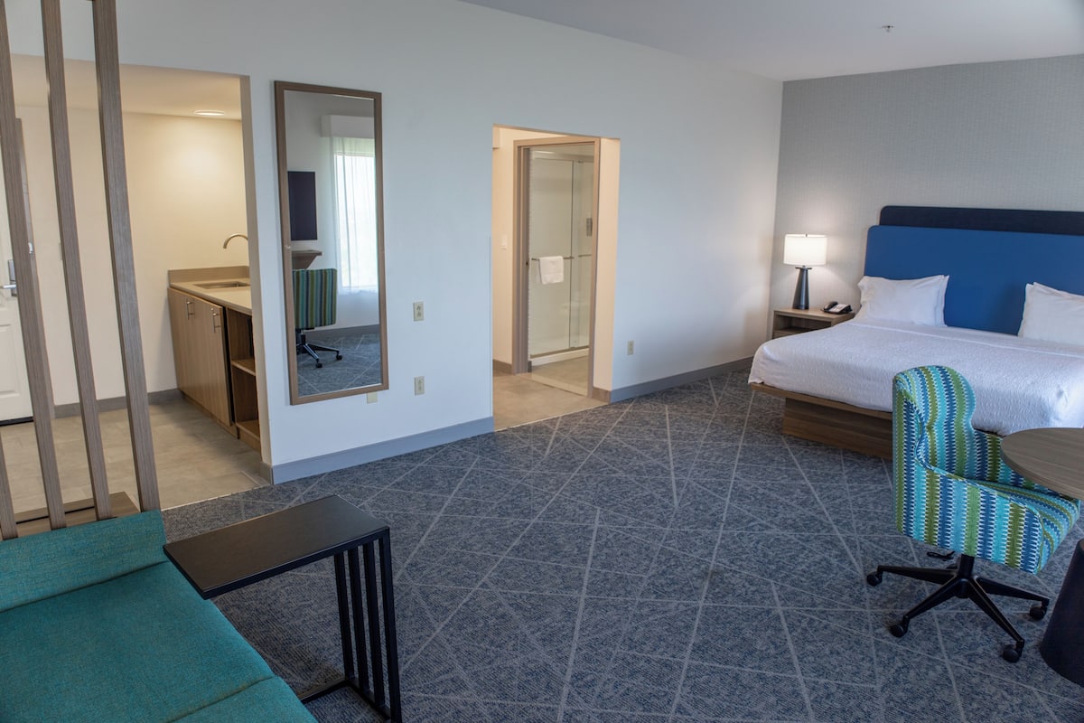 A hotel room with a bed, a desk, a chair, a mirror, and a bathroom door.