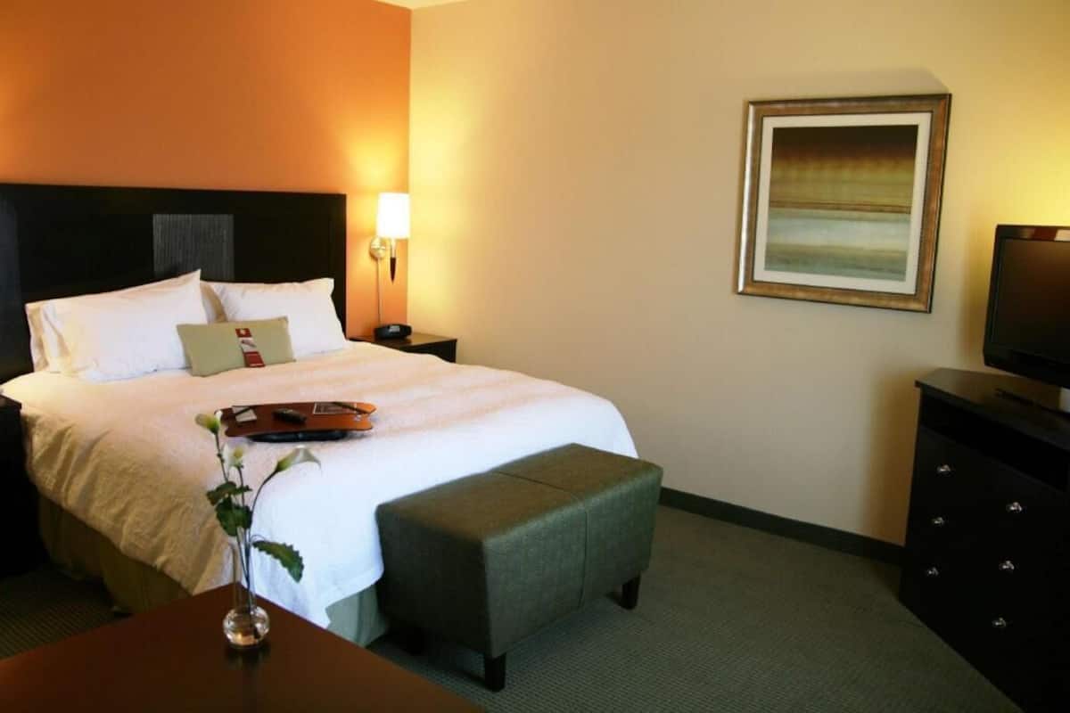 A hotel room with a bed, bedside table, lamp, TV, and a framed picture on the wall.