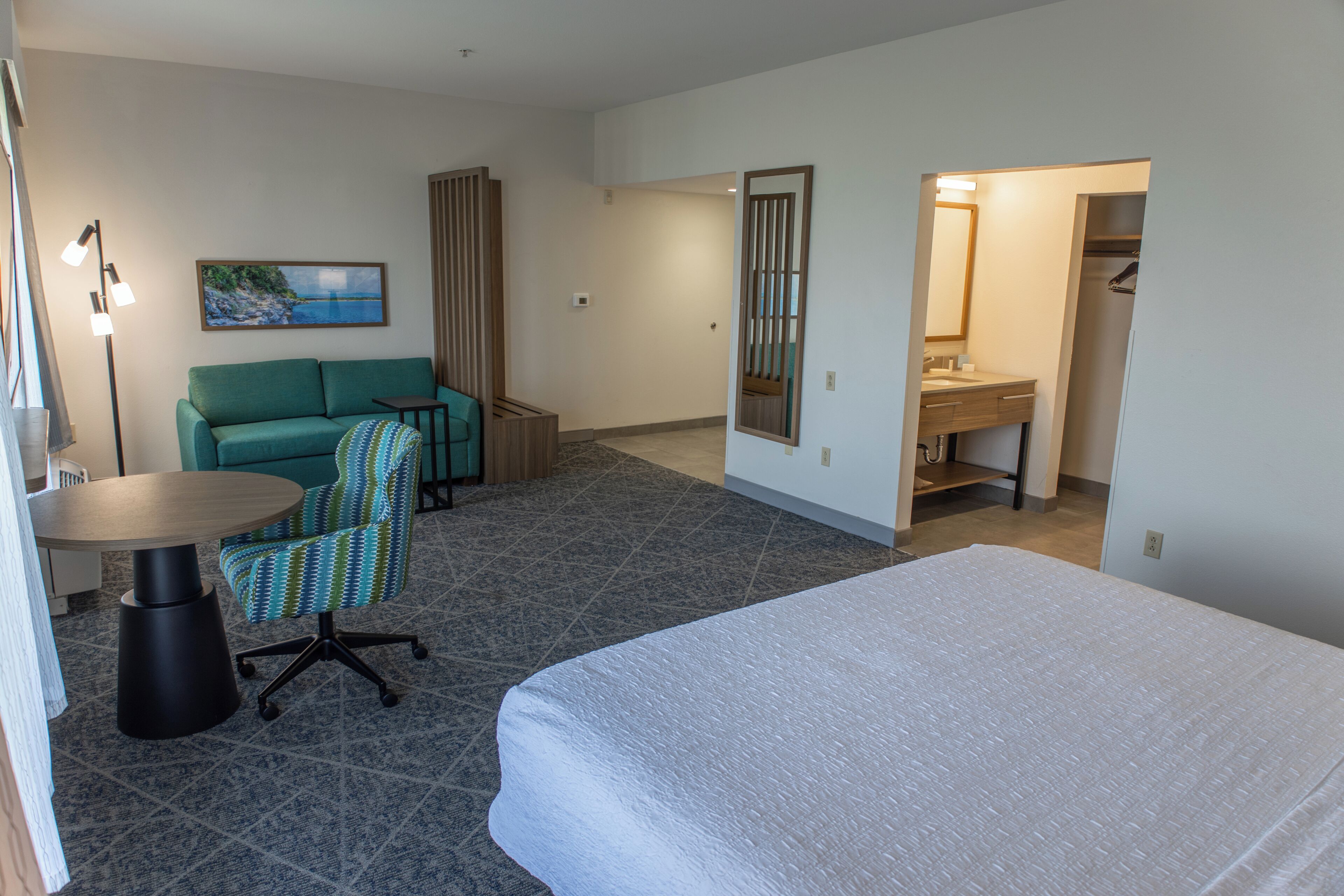 A hotel room with a bed, a sofa, a desk, a chair, and a bathroom.