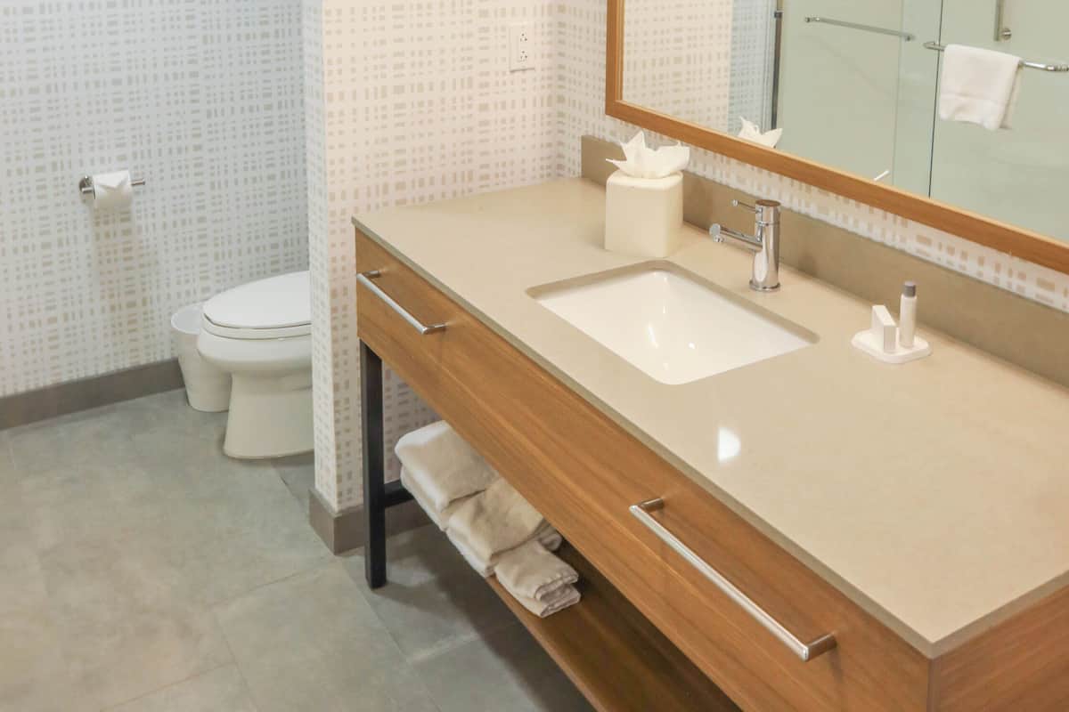 A modern bathroom with a large mirror, two sinks, a toilet, and a shower.