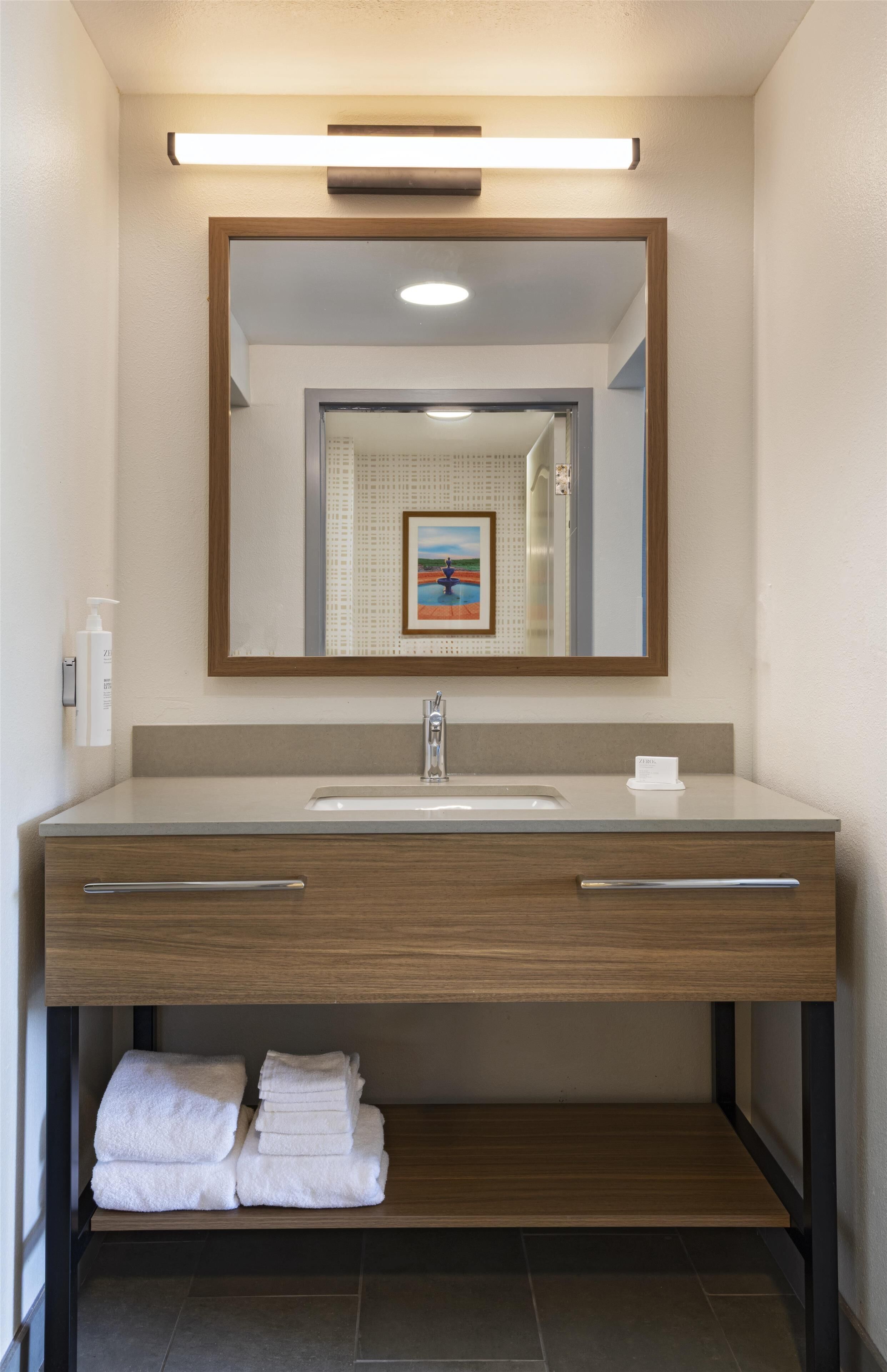 A modern bathroom with a large mirror, a sink, and a towel rack.