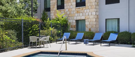 A swimming pool with lounge chairs and a table, surrounded by a fence and greenery.