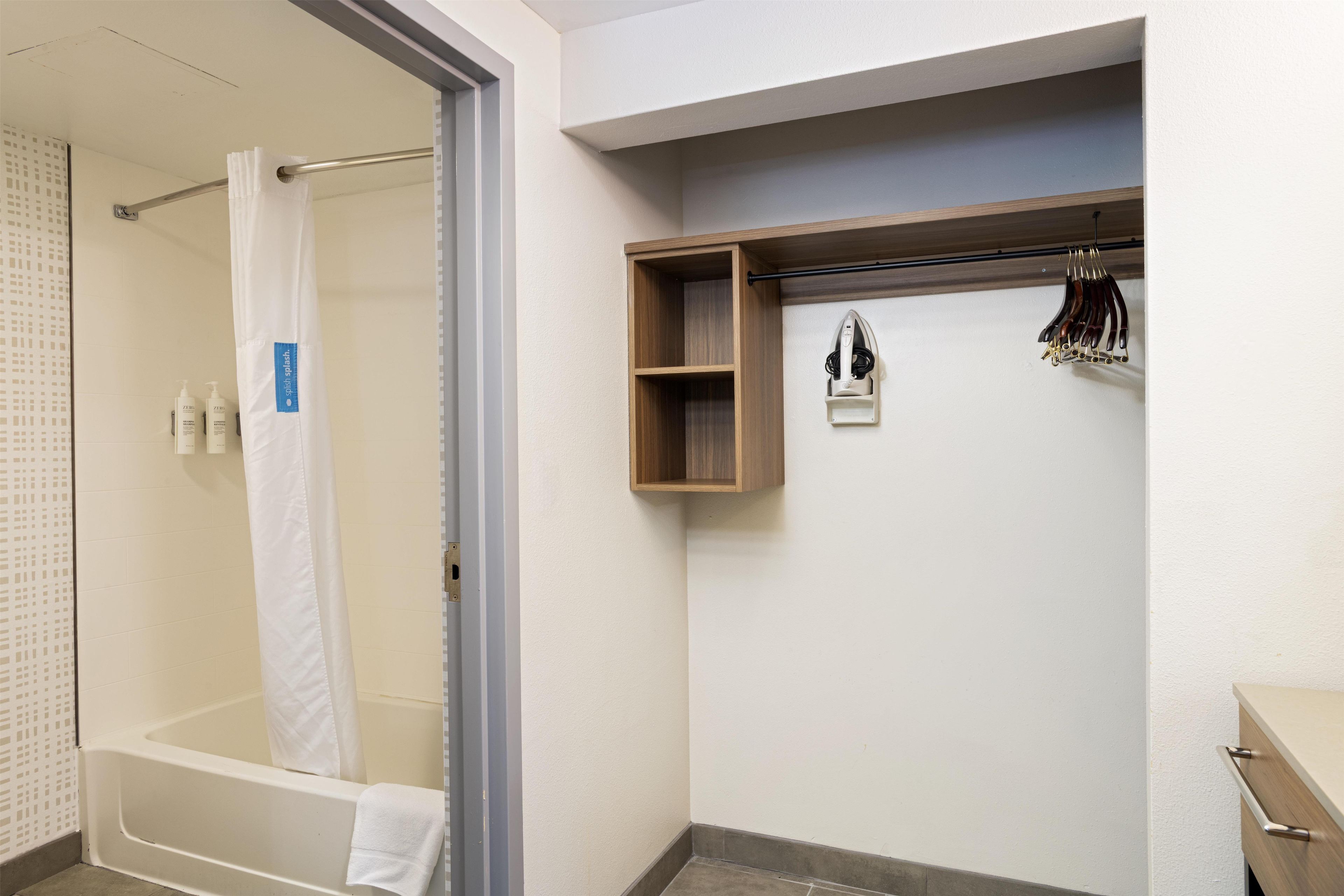 Een badkamer met een bad, douche, handdoekhouder en een plank met toiletartikelen.