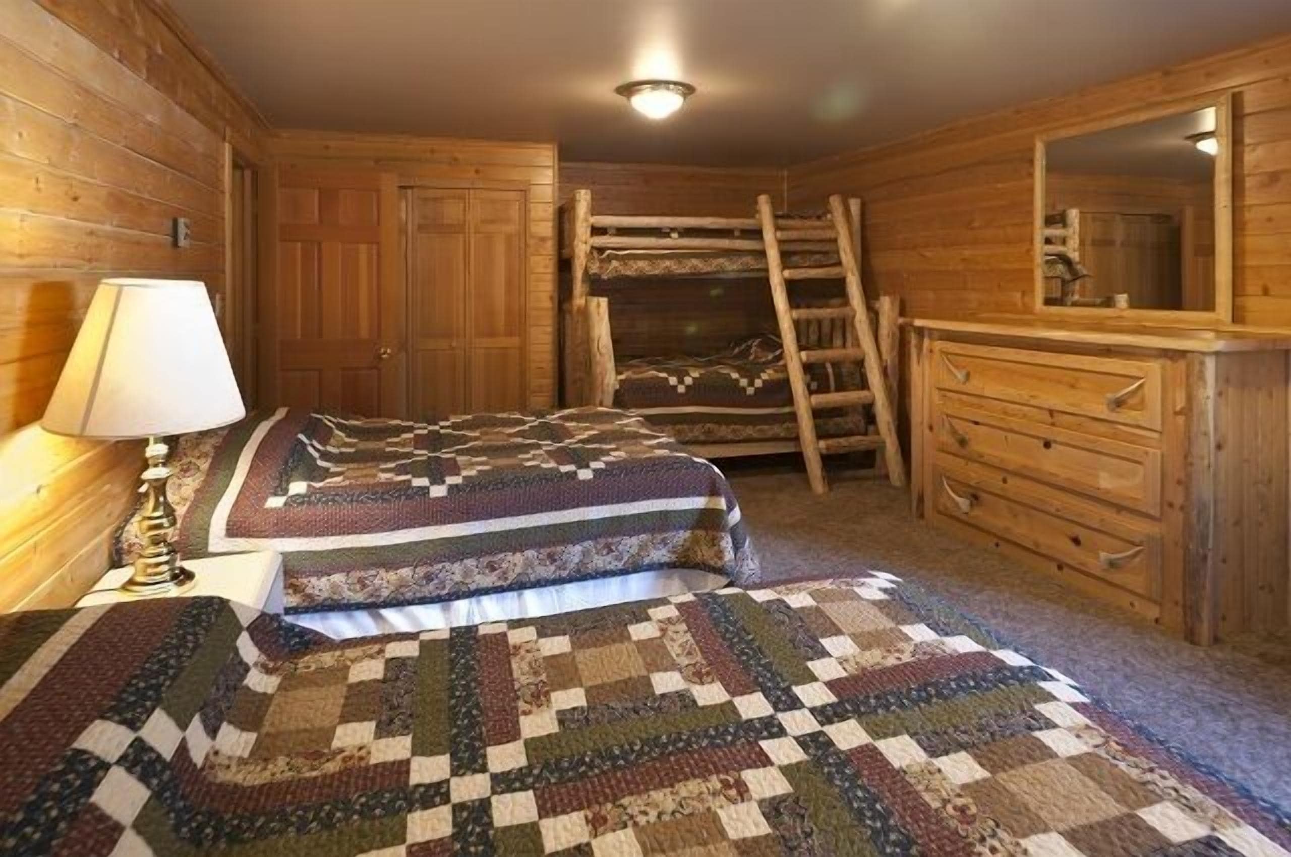A rustic wooden room with a bunk bed, a dresser, and a mirror.
