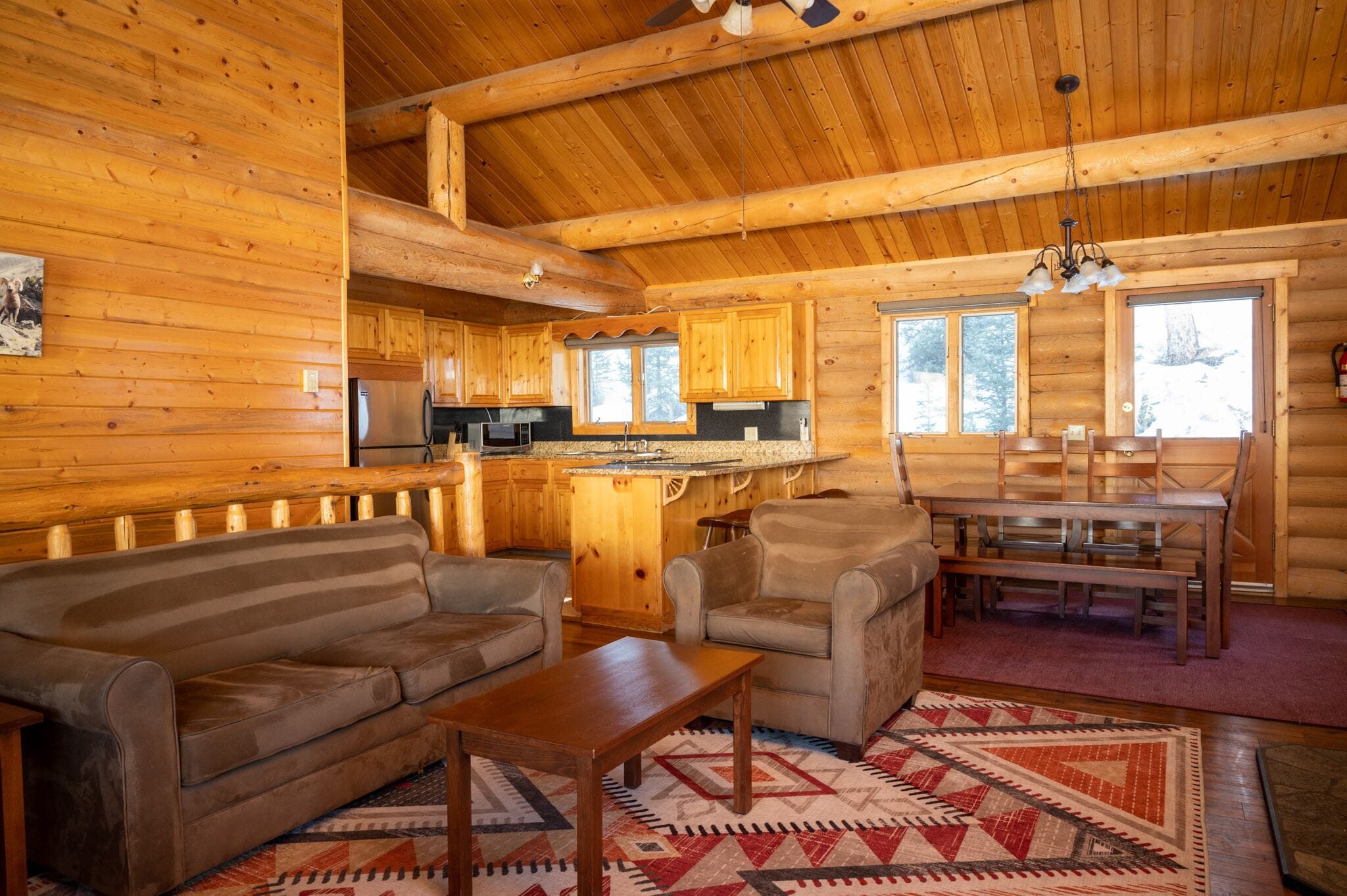 Interior de una cabaña de troncos con una sala de estar acogedora, una mesa de comedor de madera y cocina.