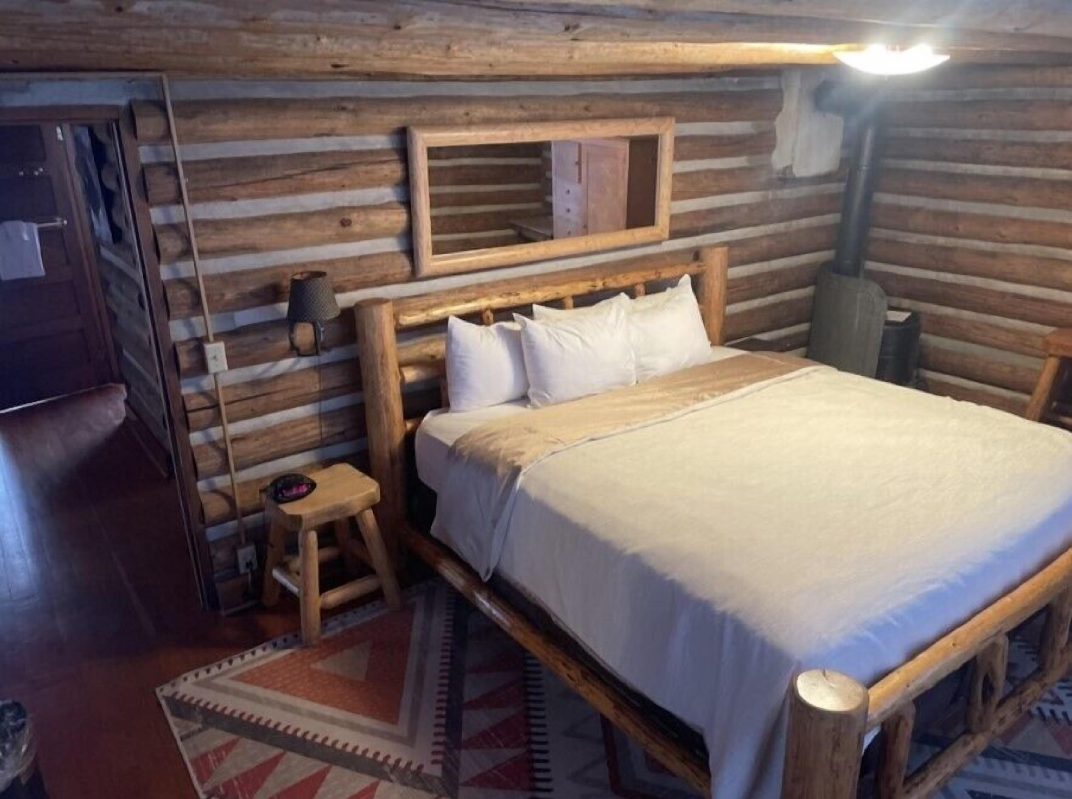 Habitación de una cabaña de madera con una cama, un mesita de noche, una lámpara y un espejo en la pared.
