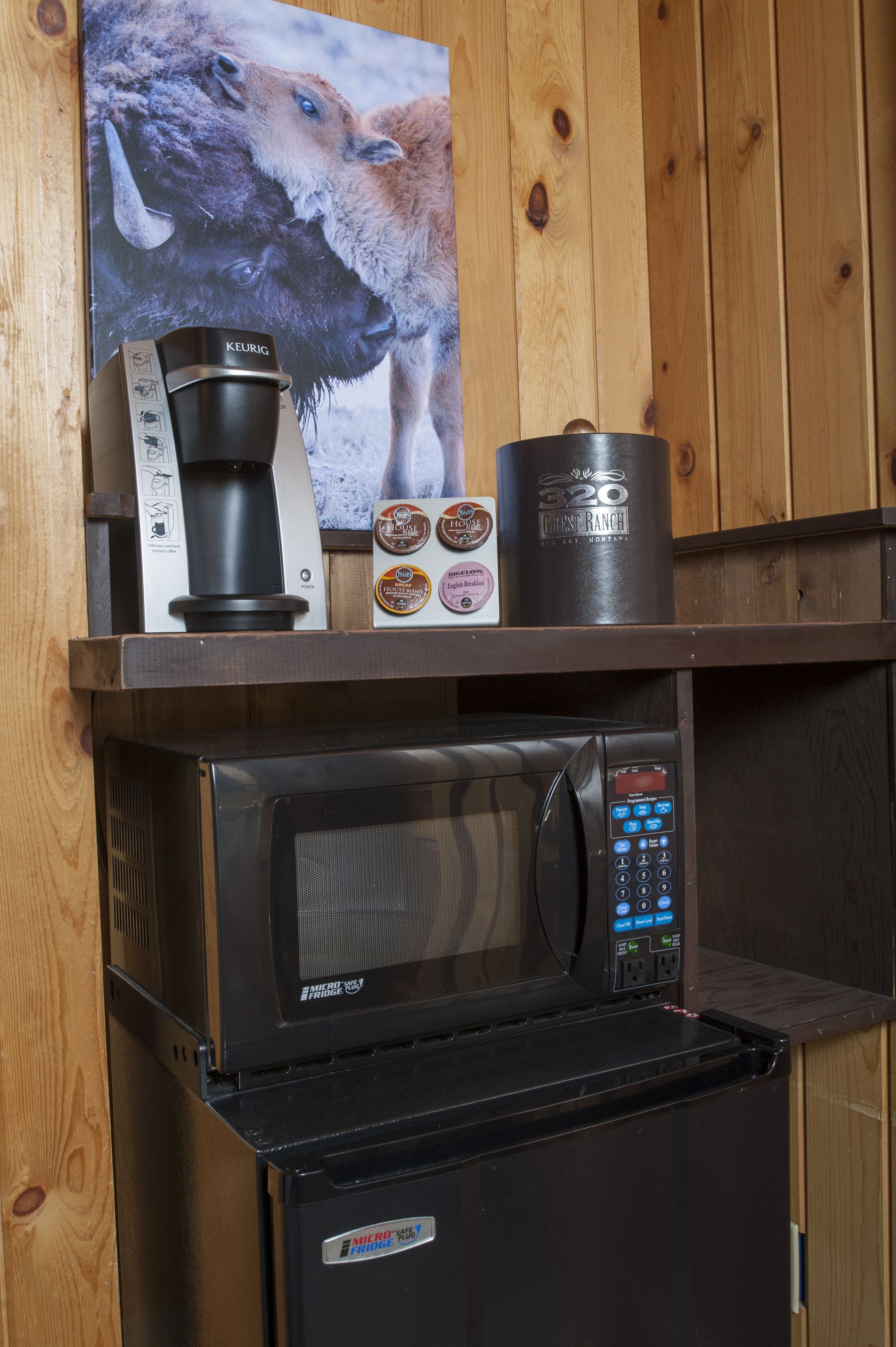 Una kitchenette con cafetera, microondas y soporte para cápsulas de café.