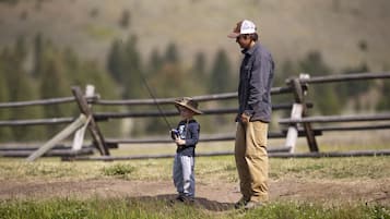 Un homme et un enfant pêchent près d’une clôture en bois, dans un champ herbeux.