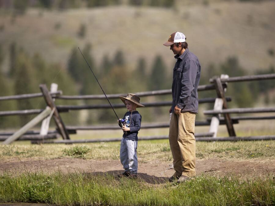 Un homme et un enfant pêchent près d’une clôture en bois, dans un champ herbeux.