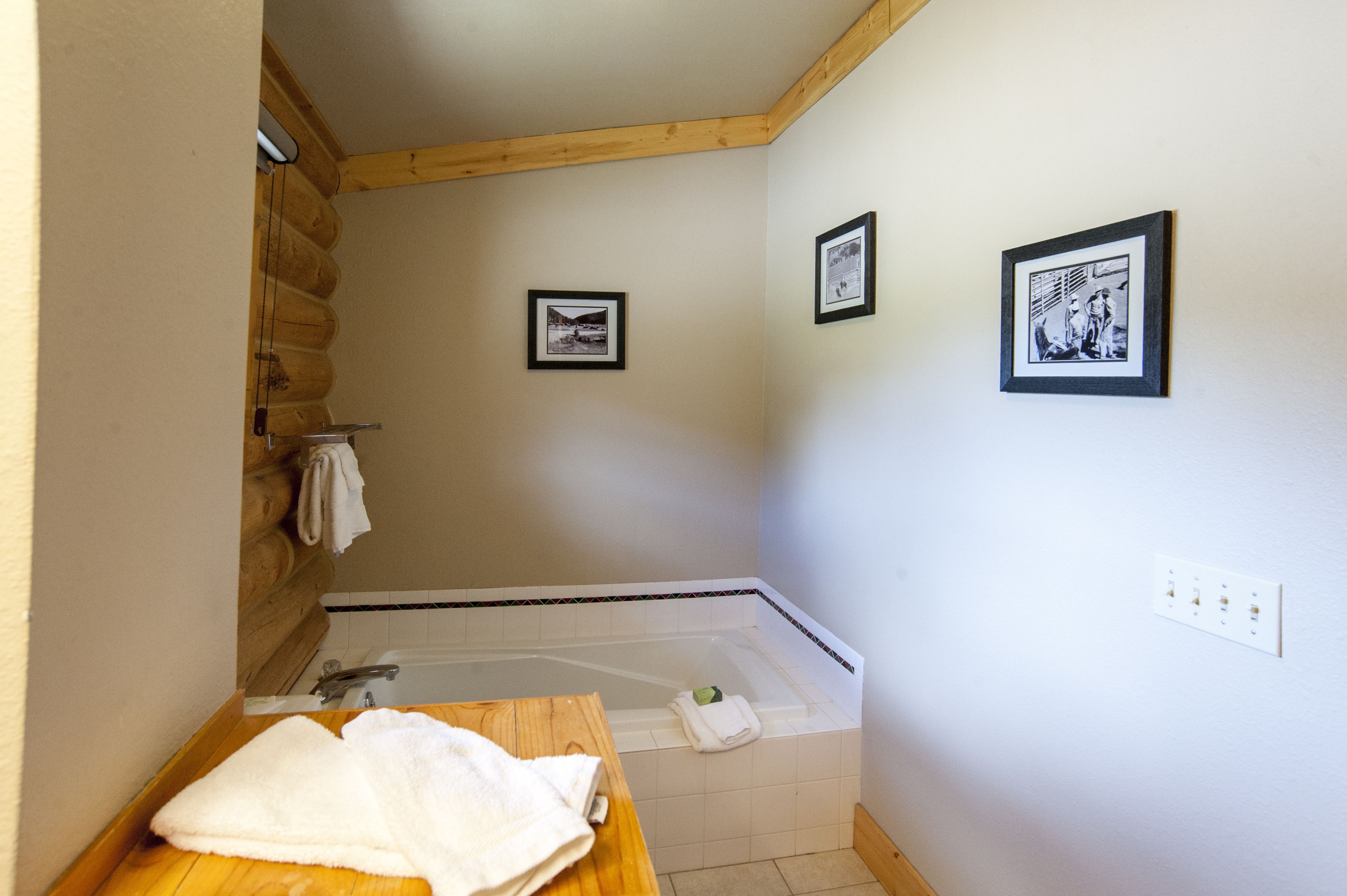 Une salle de bain avec un banc en bois, une baignoire et deux tableaux encadrés au mur.