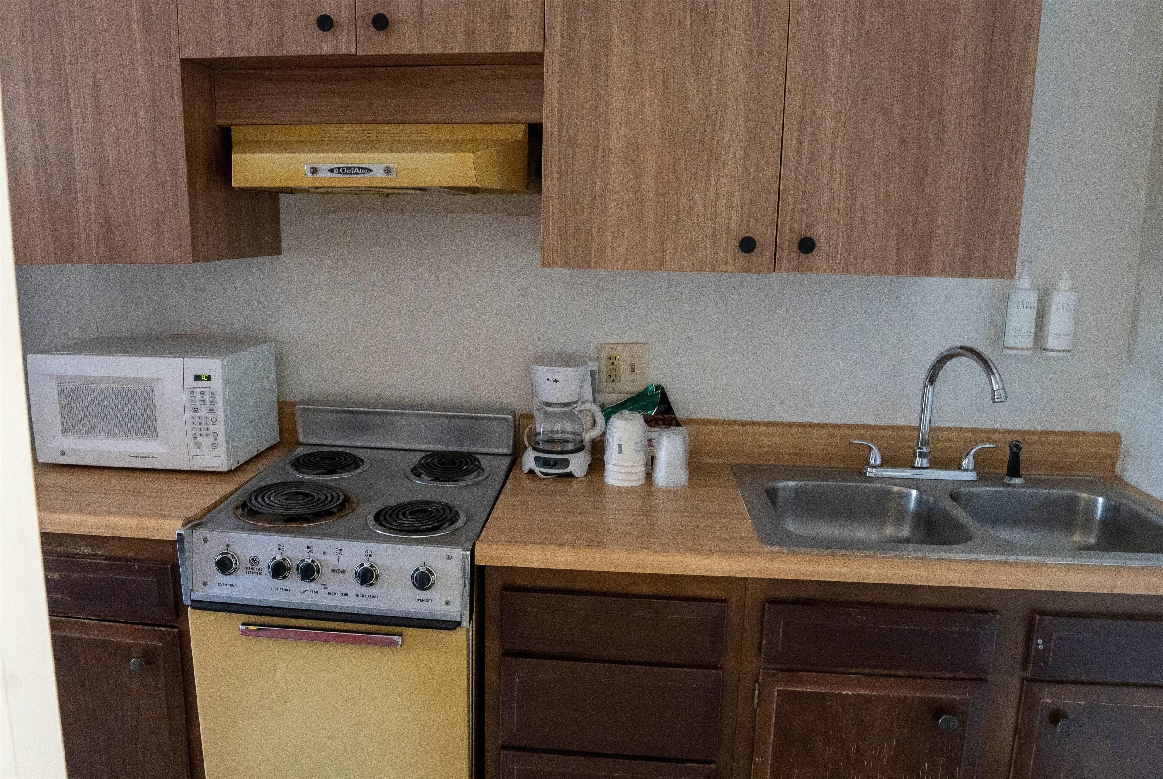 A compact kitchen with a stove, microwave, sink, and cabinets.