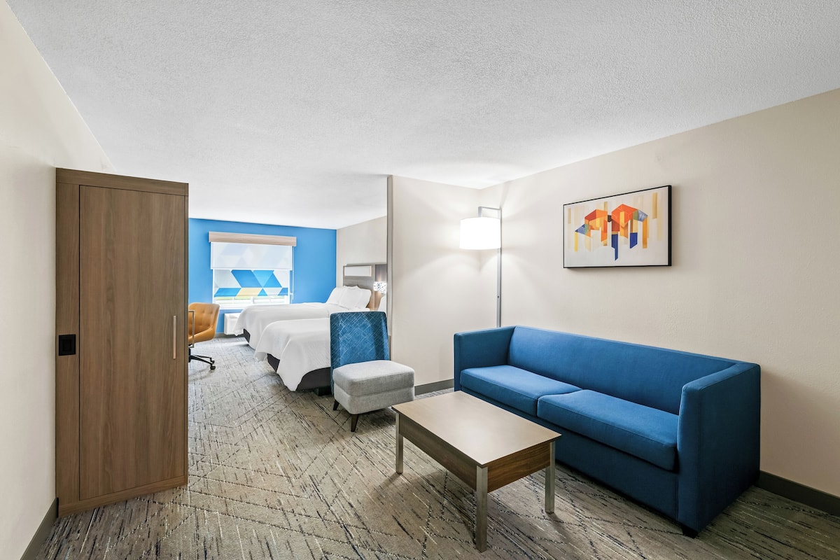 Une chambre d’hôtel avec un lit, un canapé bleu, une petite table et un tableau au mur.