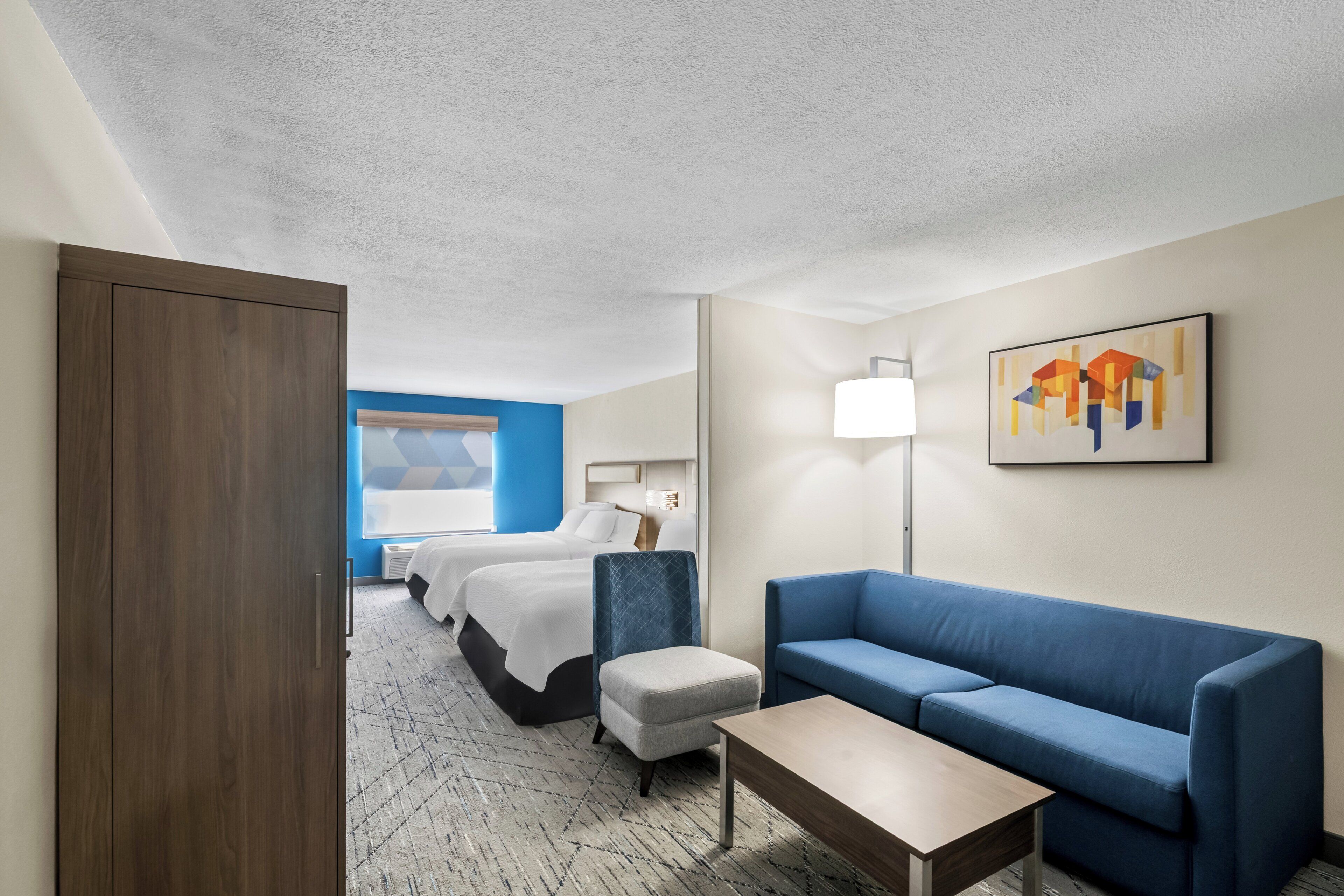 Ein Hotelzimmer mit einem Bett, einem blauen Sofa, einem Holzschrank, einem kleinen Tisch und einem Gemälde an der Wand.