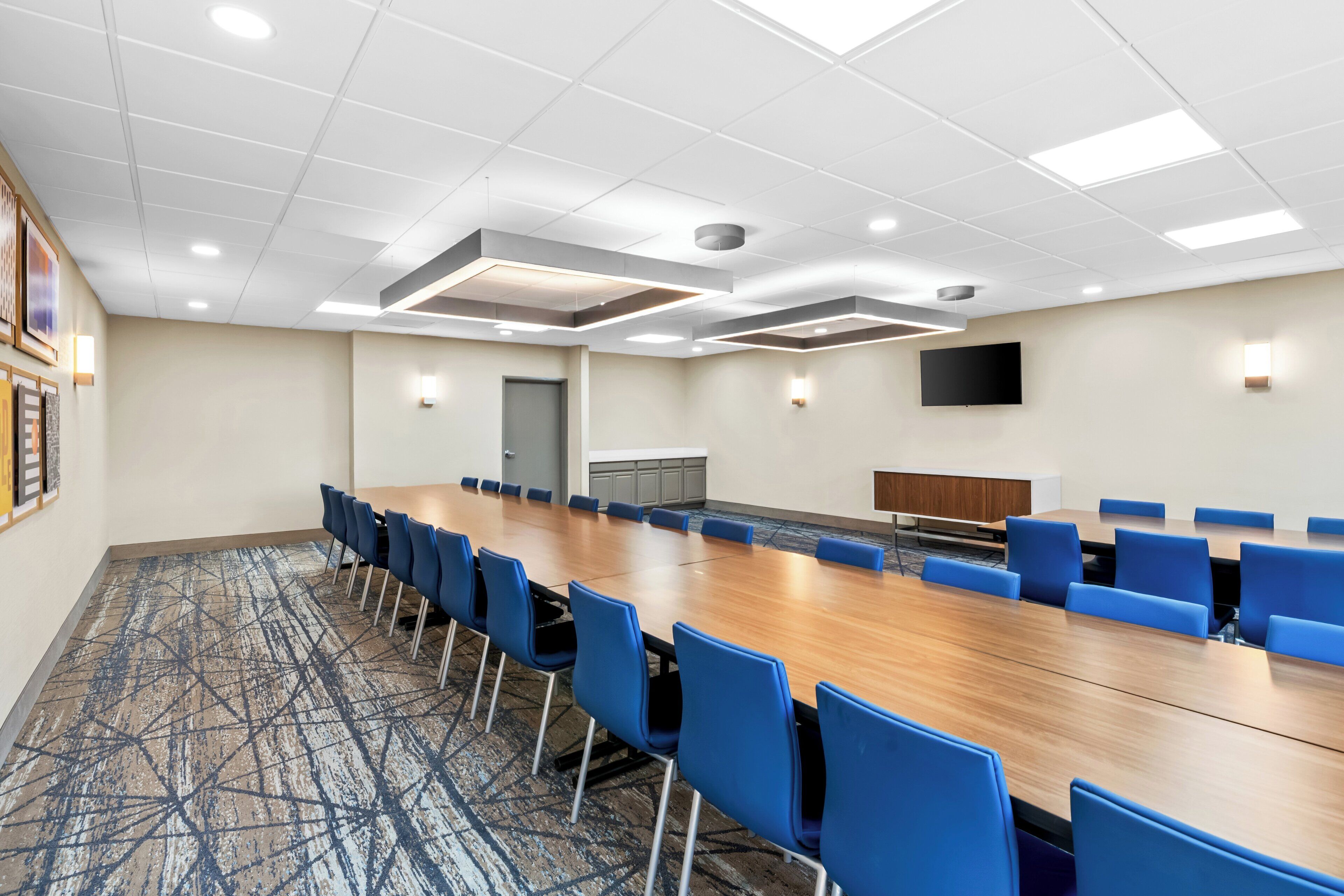 A conference room with a long table, blue chairs, and a patterned carpet.
