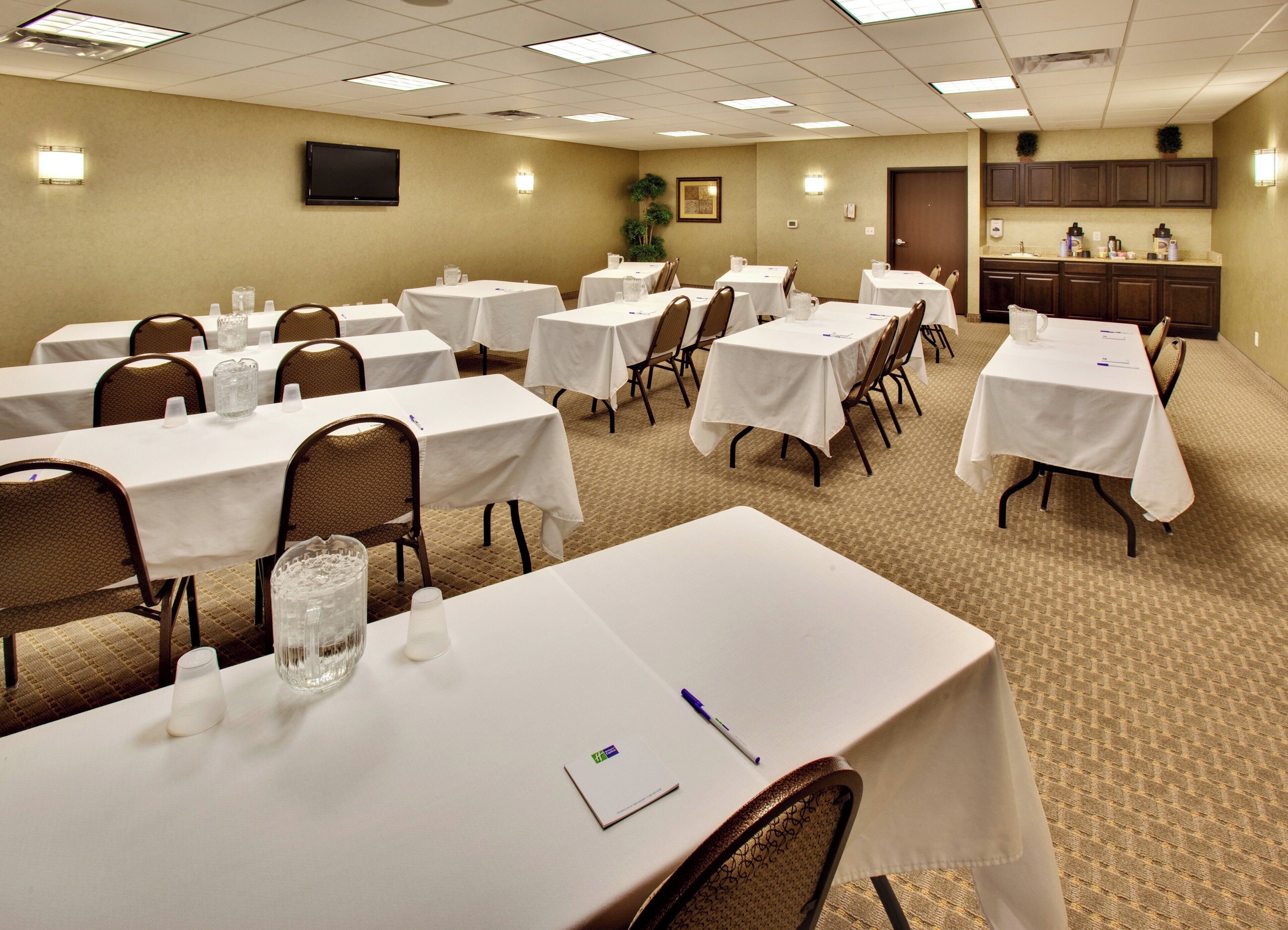 A conference room with multiple tables, chairs, and a kitchenette area.