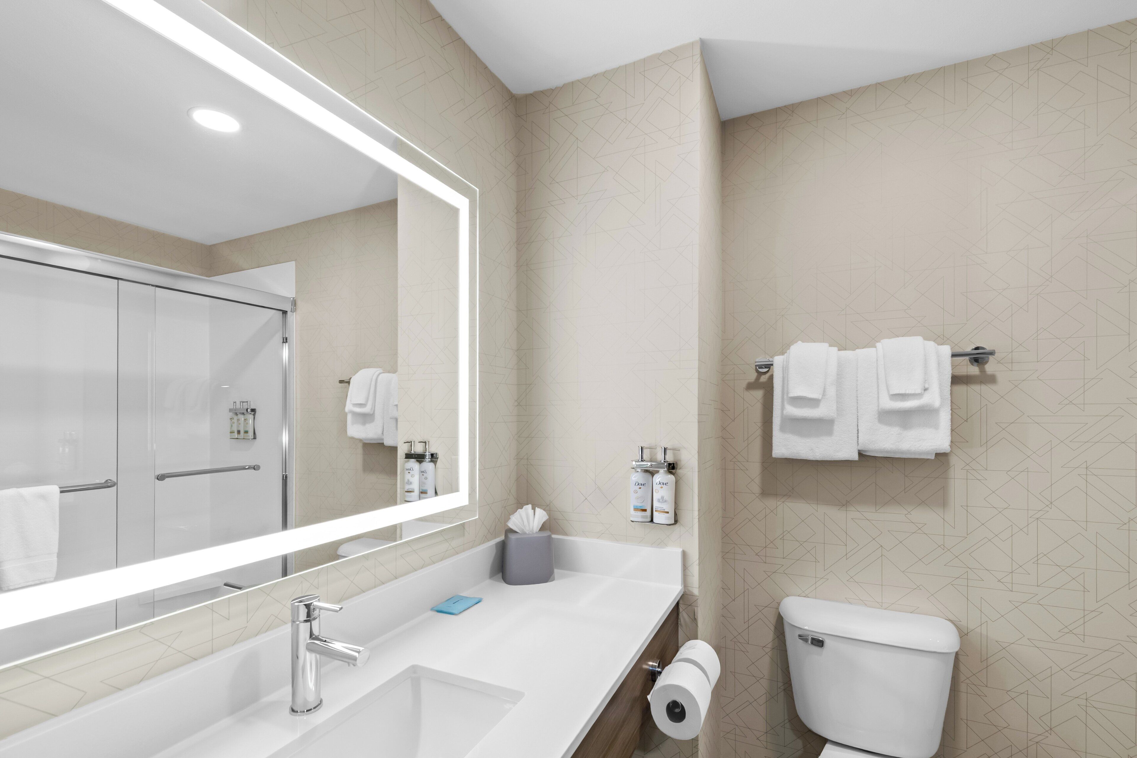A modern bathroom with a large mirror, a white sink, a toilet, and a towel rack.