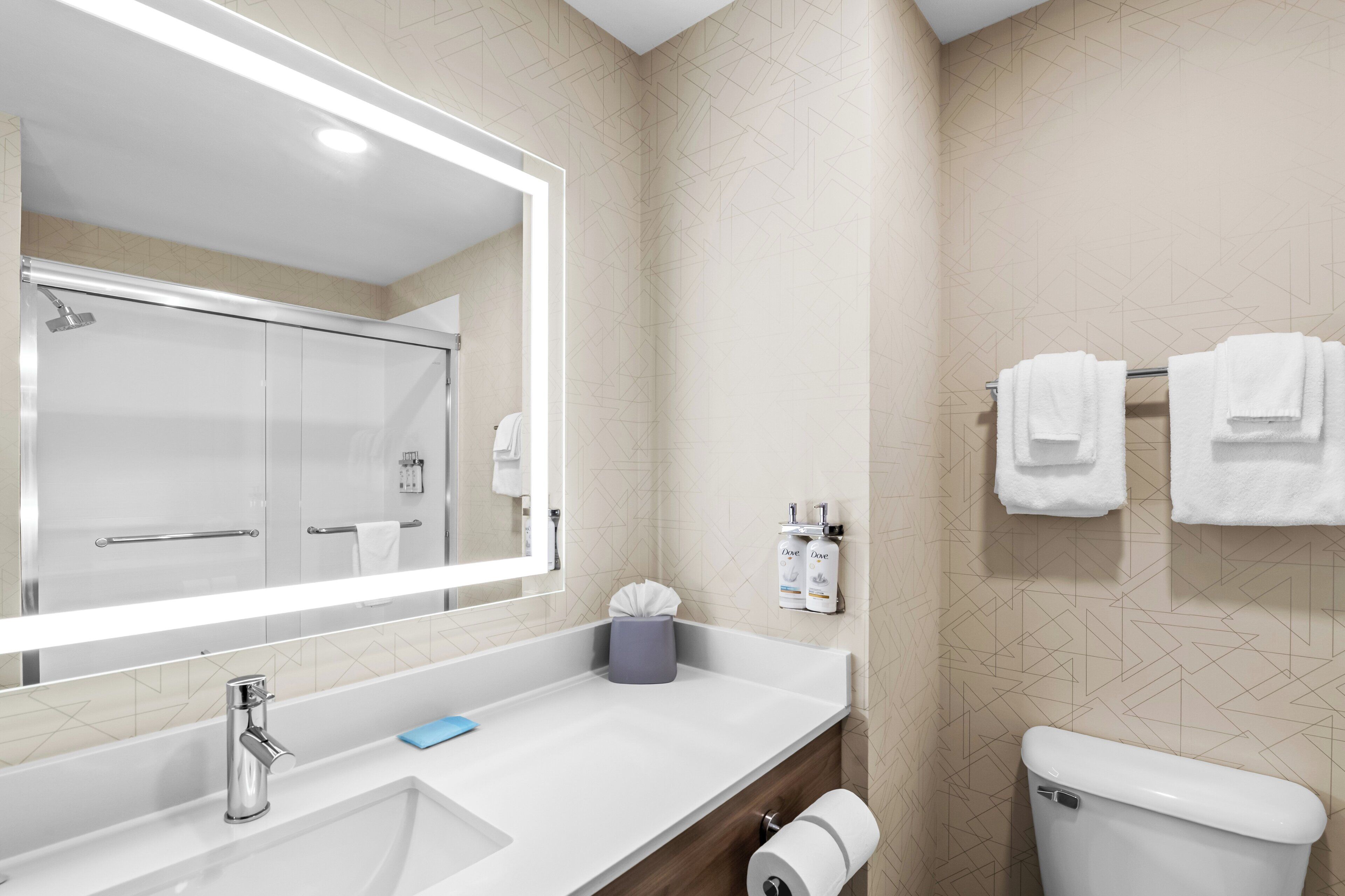 A modern bathroom with a large mirror, a sink, a toilet, and two towels hanging on a rack.