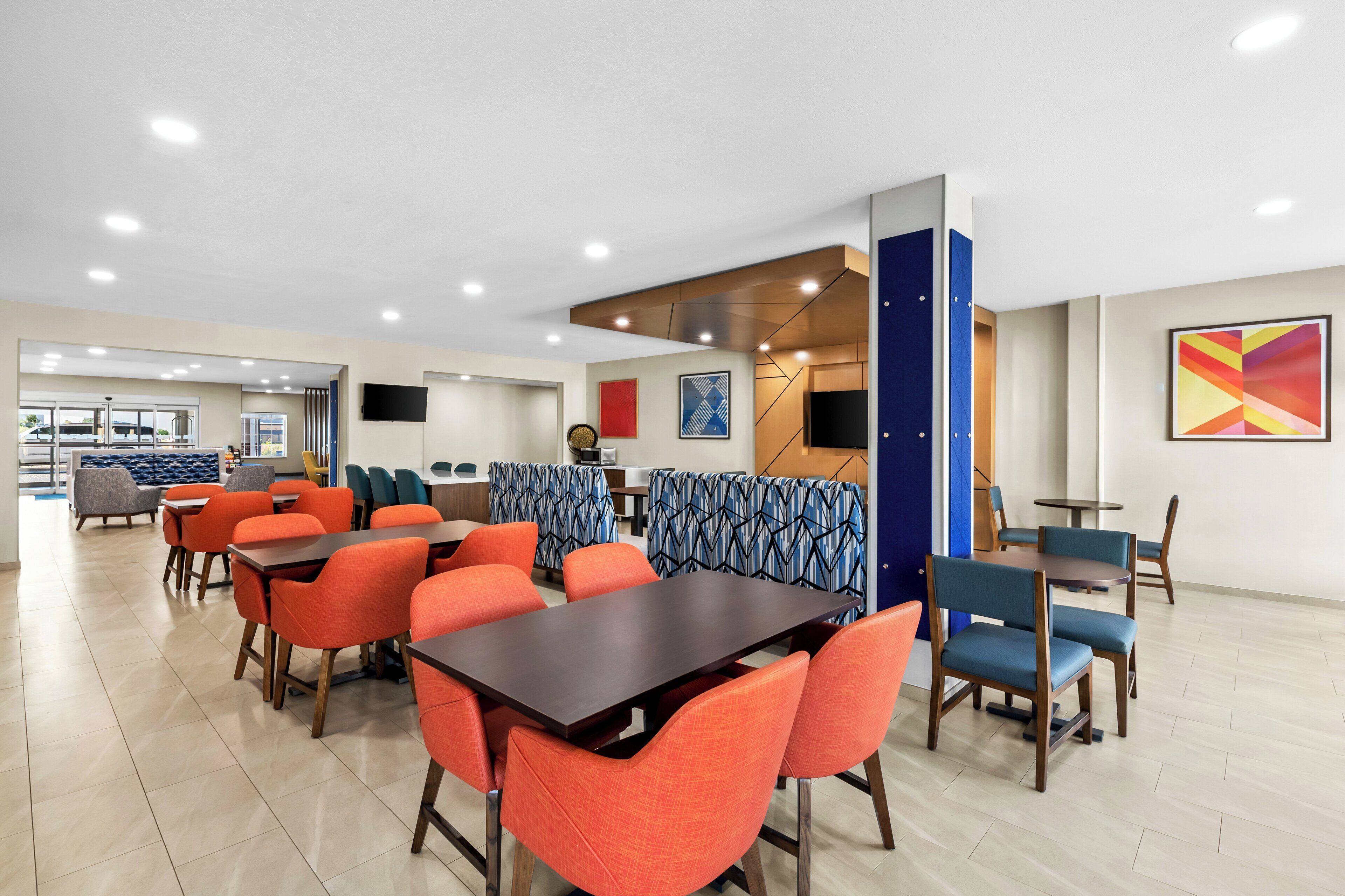 A modern dining area with multiple tables and chairs, a counter, and a television on the wall.