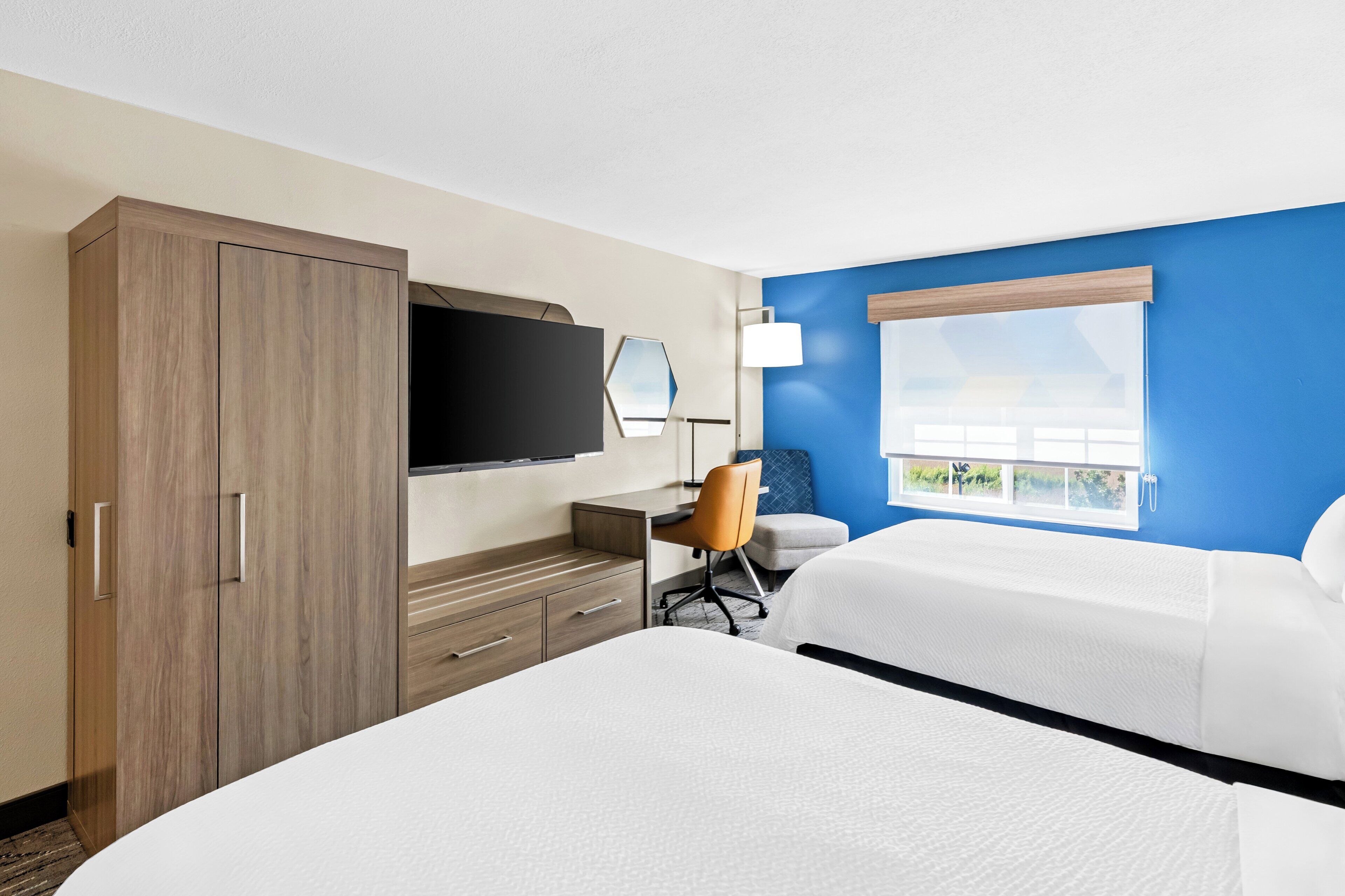 A hotel room with a large bed, a desk with a chair, a television, and a window with a view.