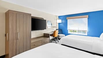 A hotel room with a large bed, a desk with a chair, a television, and a window with a view.