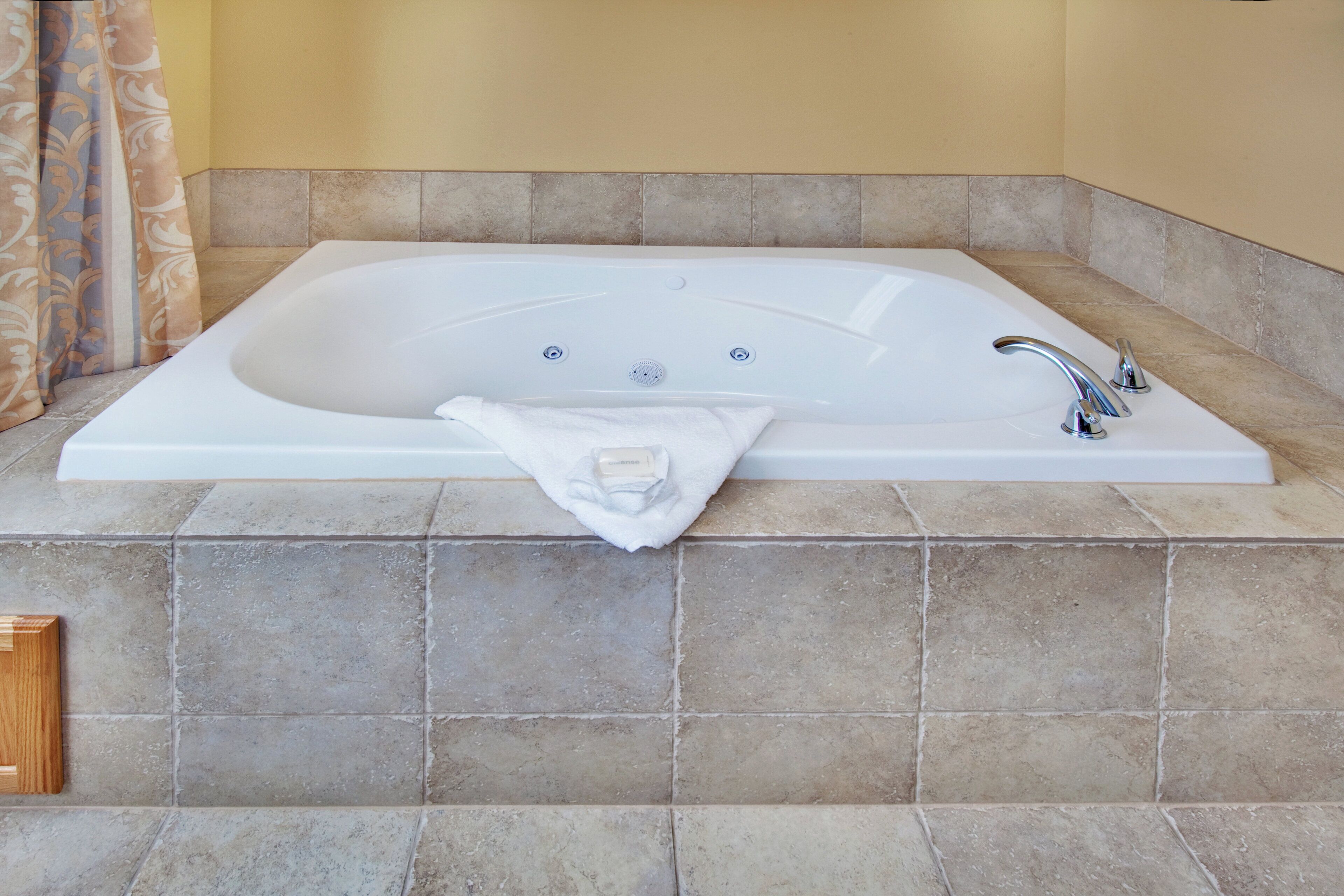 A large rectangular bathtub with a single faucet and two drain holes, placed on a tiled floor against a wall.