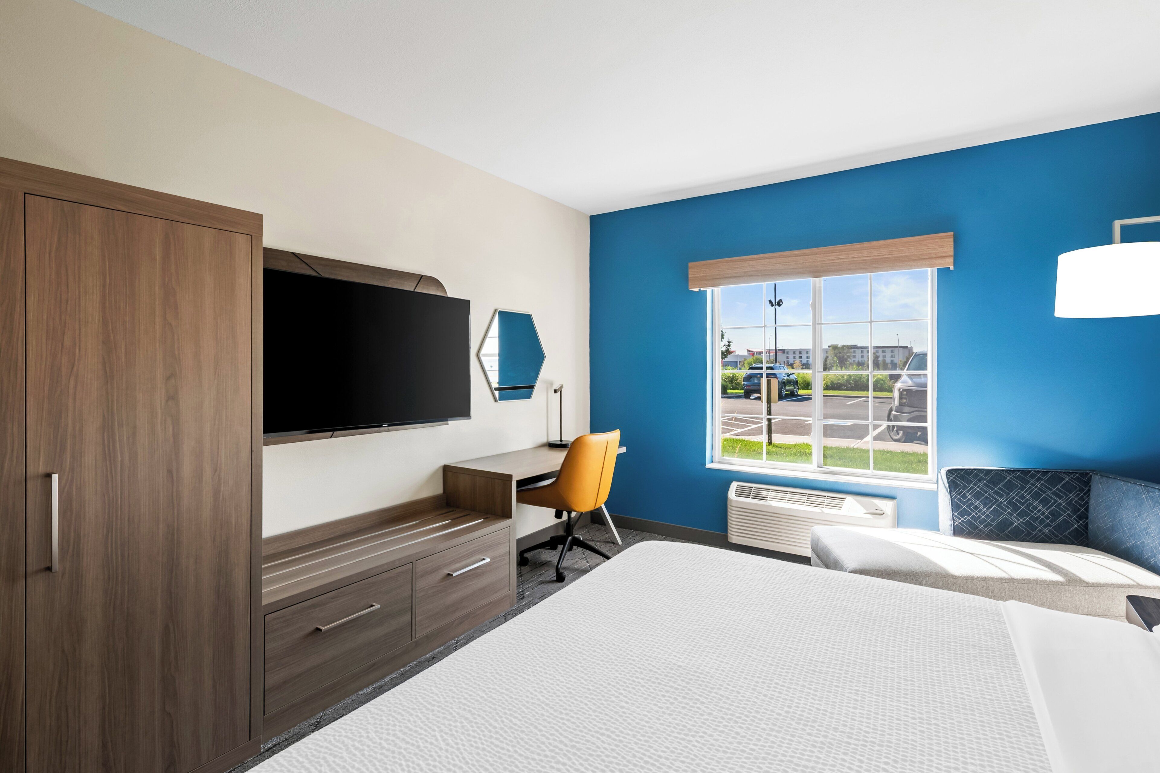 A hotel room with a bed, a desk with a chair, a television, and a window with a view of the outside.