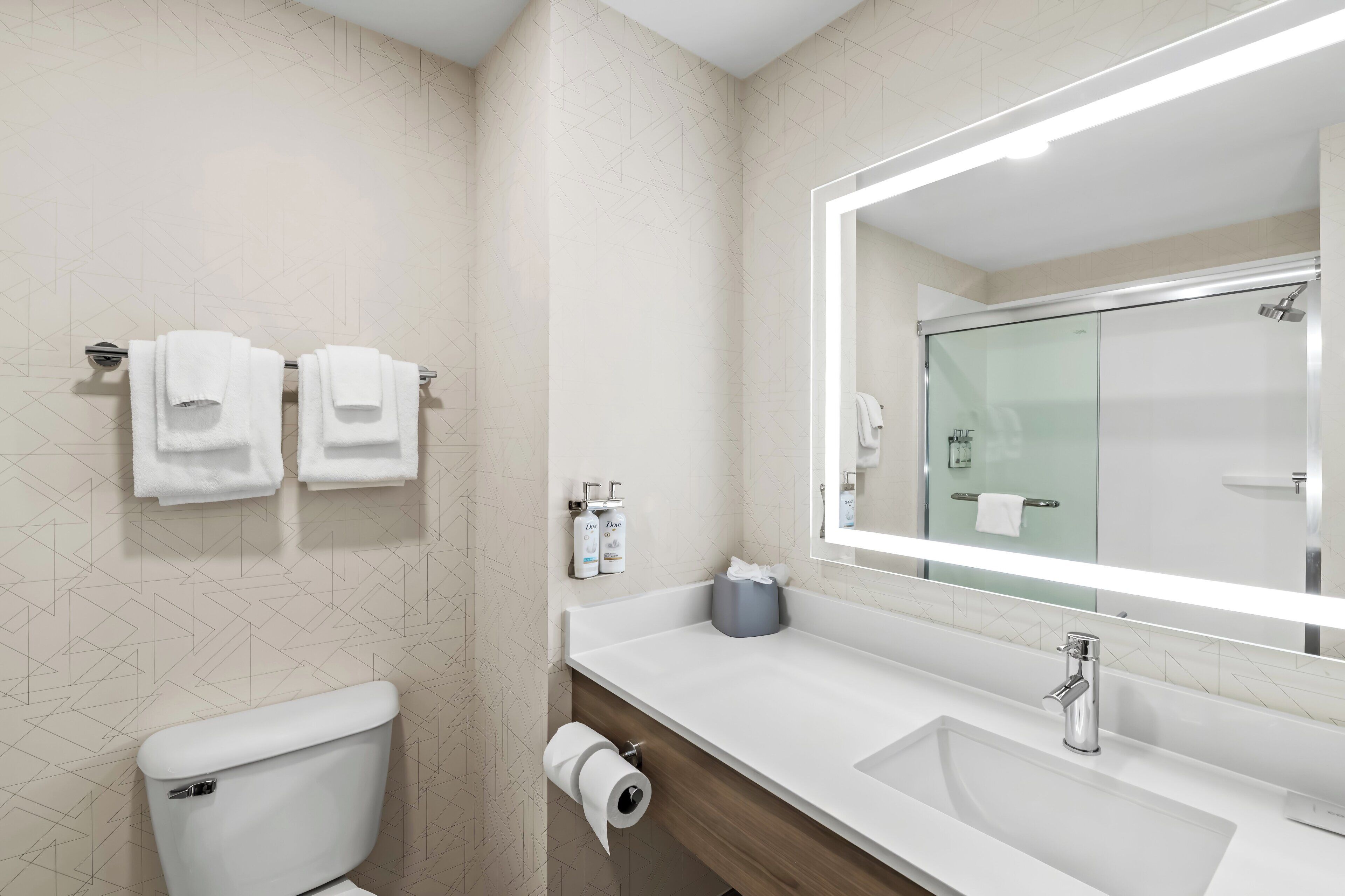 A modern bathroom with a toilet, sink, and a large mirror.