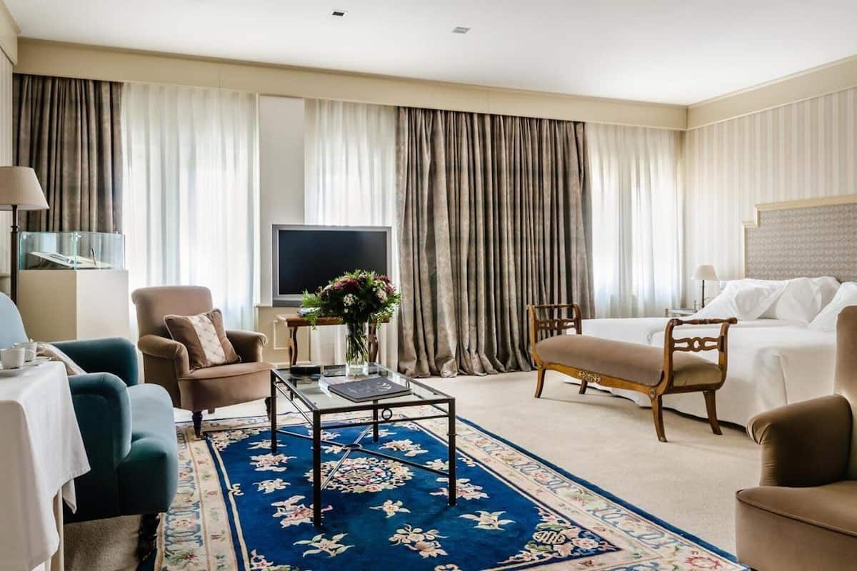 Una habitación de hotel con una cama grande, un sofá, una silla, una mesita de centro y un televisor.