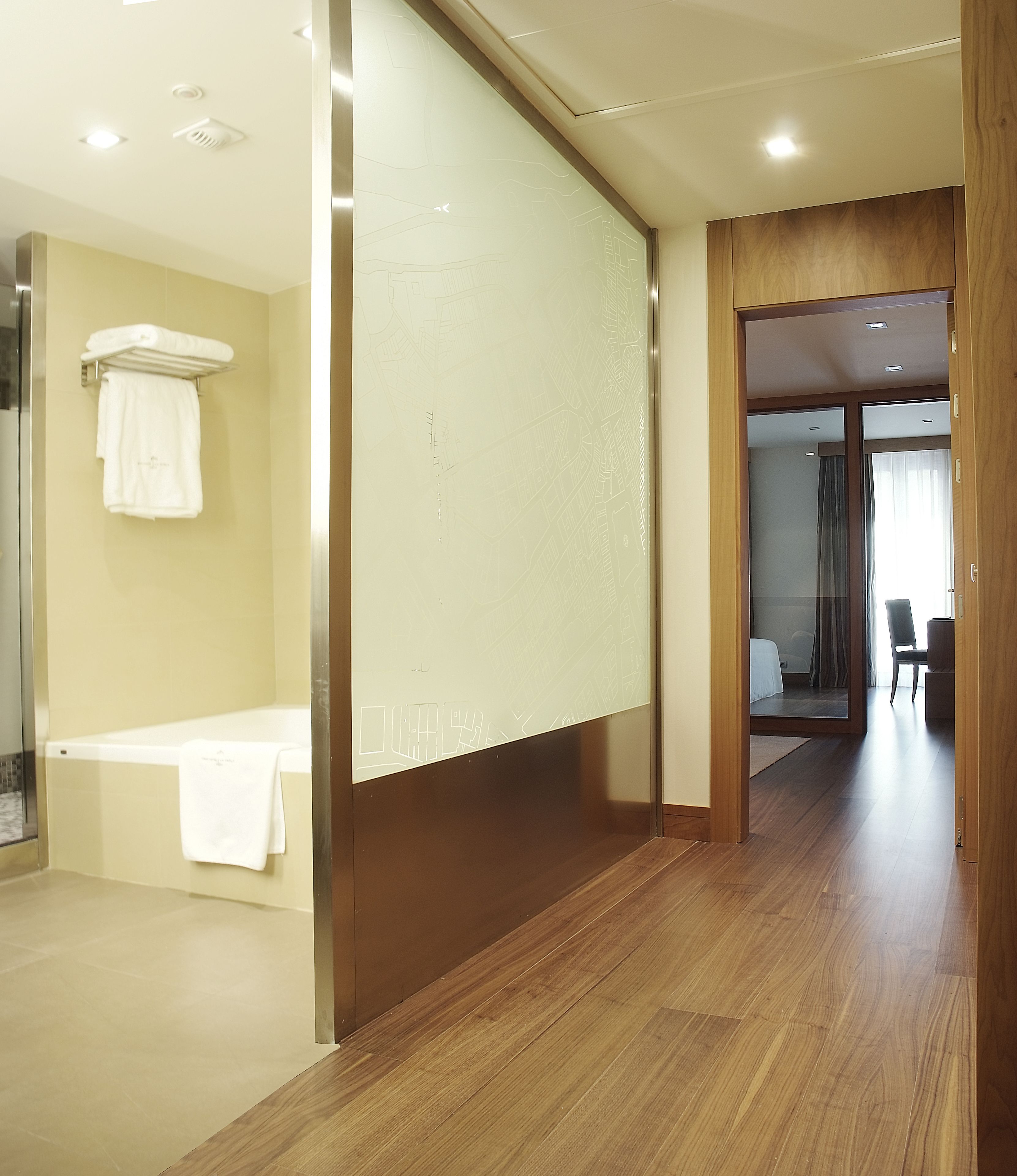 Una habitación de hotel moderna con suelo de madera, una bañera y zona de baño visible.