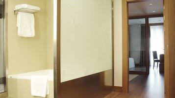 Una habitación de hotel moderna con suelo de madera, una bañera y zona de baño visible.