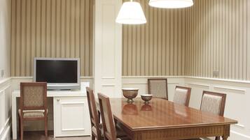Un comedor con mesa de madera, sillas, televisor y luces colgantes.