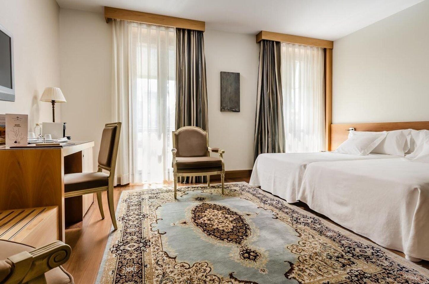 Une chambre d’hôtel avec un lit, un bureau doté d’une lampe, une chaise et un grand tapis.