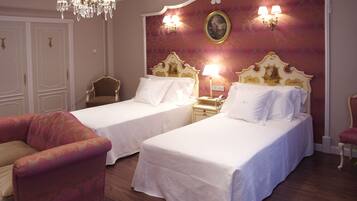 A hotel room with two beds, a chandelier, a red patterned wall, and a painting.