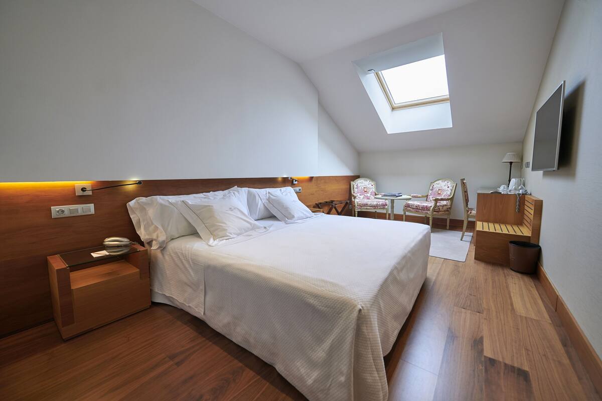 Un dormitorio con cama, mesita de noche, lámpara, silla y una pequeña mesa con lámpara.