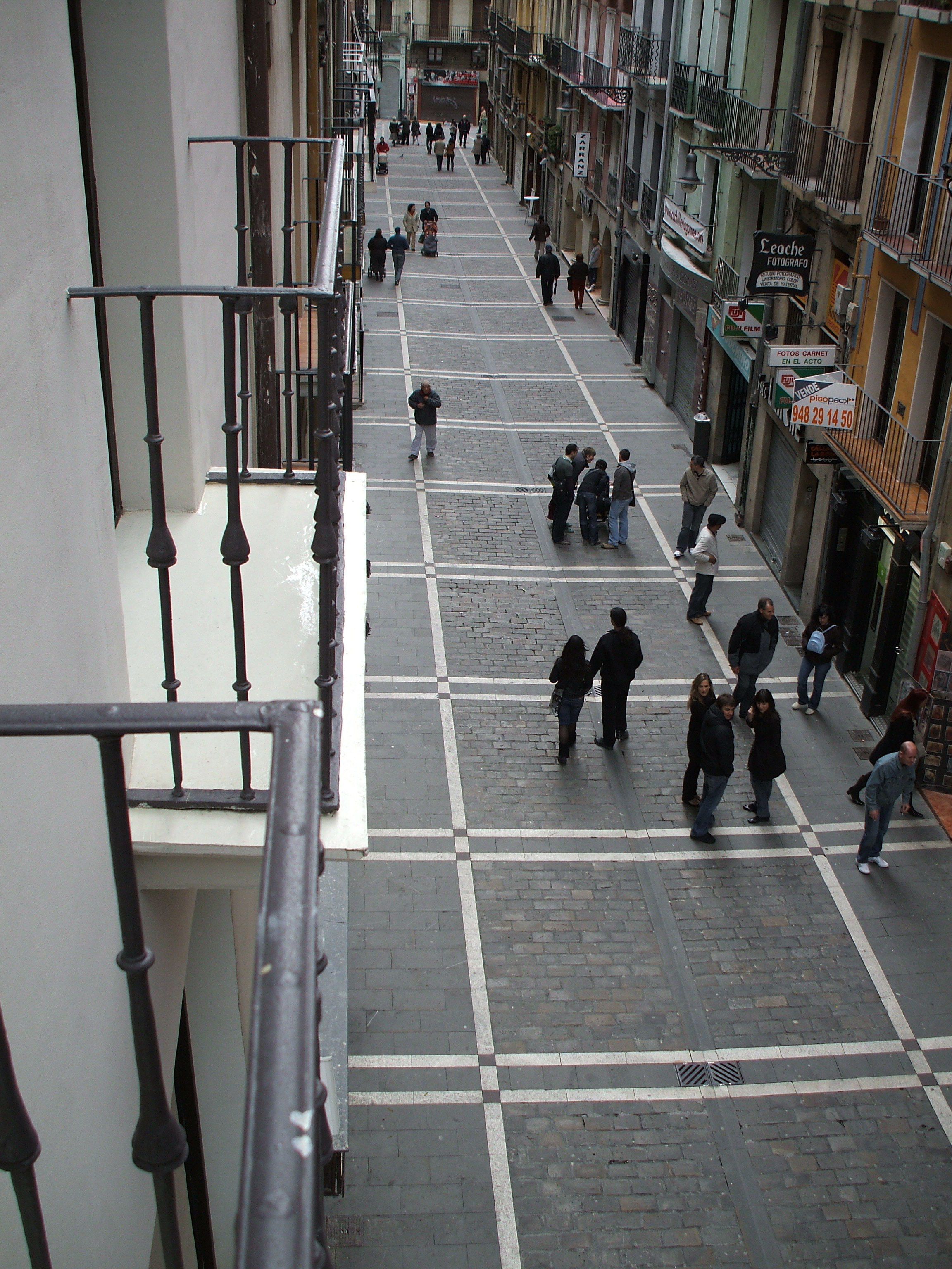 Una calle peatonal flanqueada por edificios, con pavimento de baldosas y una barandilla de metal.