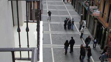 Una calle peatonal flanqueada por edificios, con pavimento de baldosas y una barandilla de metal.