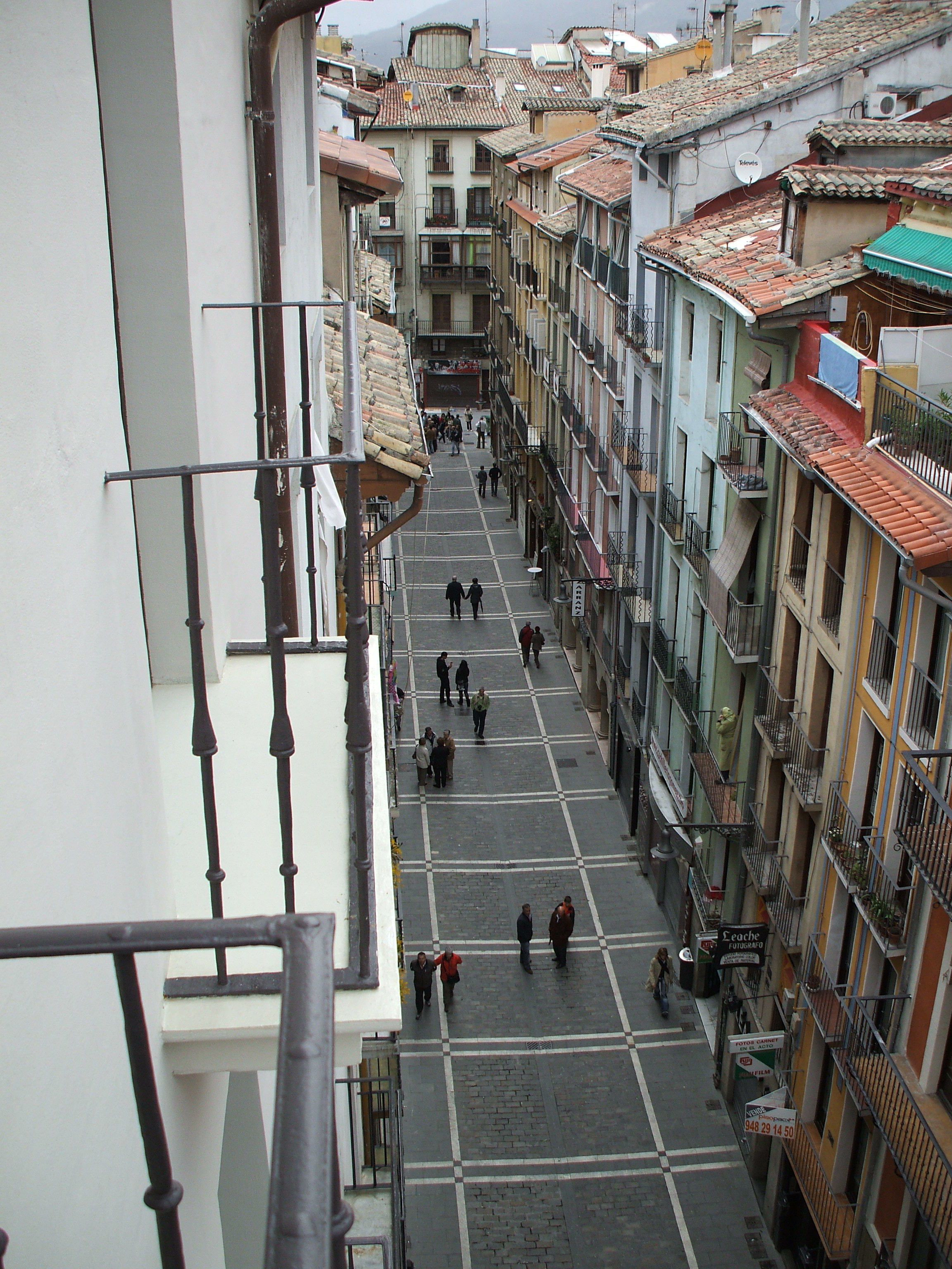 Una calle estrecha flanqueada por edificios de varios pisos, con balcones y una acera.