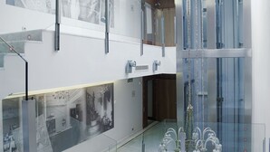 Un moderno vestíbulo de hotel con un ascensor de cristal, una escalera y una pared con fotografías históricas.