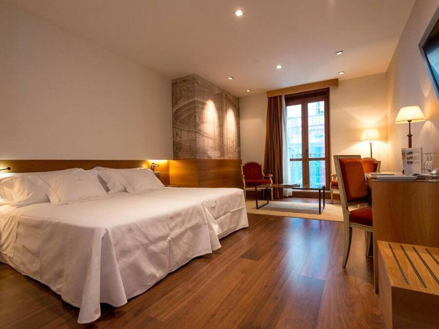 Ett hotellrum med en stor säng, ett skrivbord med en stol, en TV och ett fönster med gardiner.
