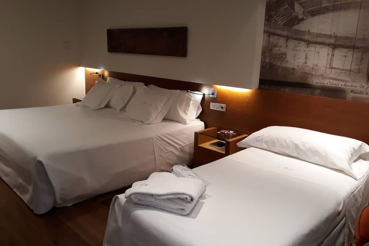 Una habitación de hotel con dos camas, una mesita de noche y una lámpara fijada a la pared.