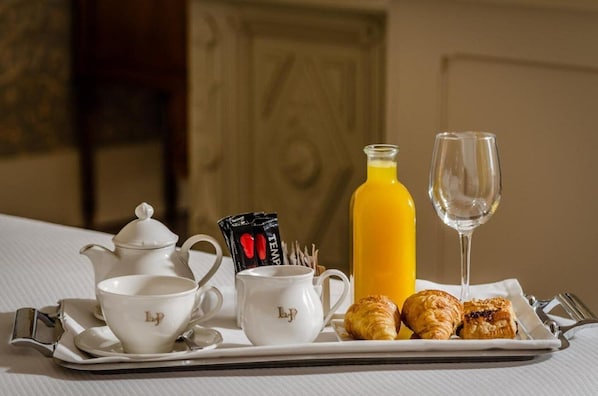 Bandeja de desayuno con cruasanes, una botella de jugo de naranja, una copa de vino y un juego de tazas de té blancas con una tetera.