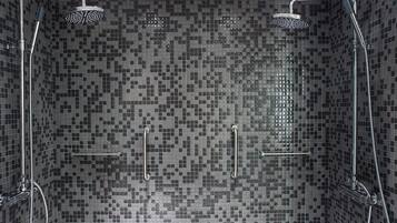 Un área de ducha con paredes de mosaicos, dos cabezales de ducha manuales y un accesorio de ducha manual.