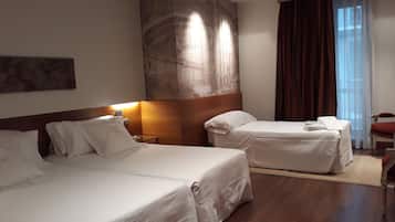 Habitación de hotel con dos camas, un mural grande en la pared, una mesita de noche y una ventana con cortinas.